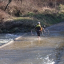 A cyclist crosses a flooded New River on foot, bike in hand.